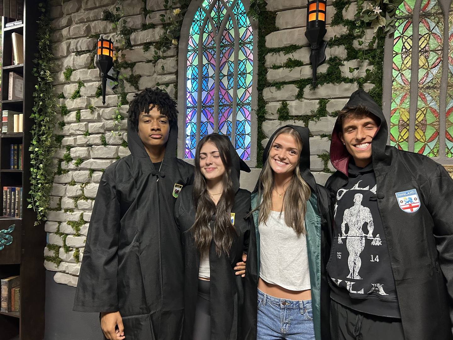 Guests in hooded robes standing before the stained glass window inside Griffin's Door escape room